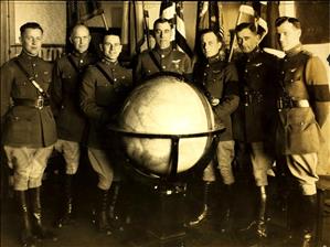 Seven white men in military uniform pose for the camera with a large globe in front of them